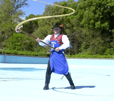 A person in a tartan vest and top-hat raises their whip dramatically into the air